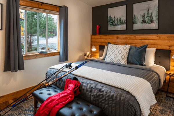 ICozy cabin bedroom with a neatly made bed, warm wood accents, soft lighting, and peaceful forest views through the window.