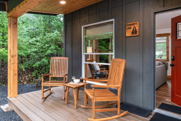 Cozy cabin porch with wooden chairs and peaceful views of trees.