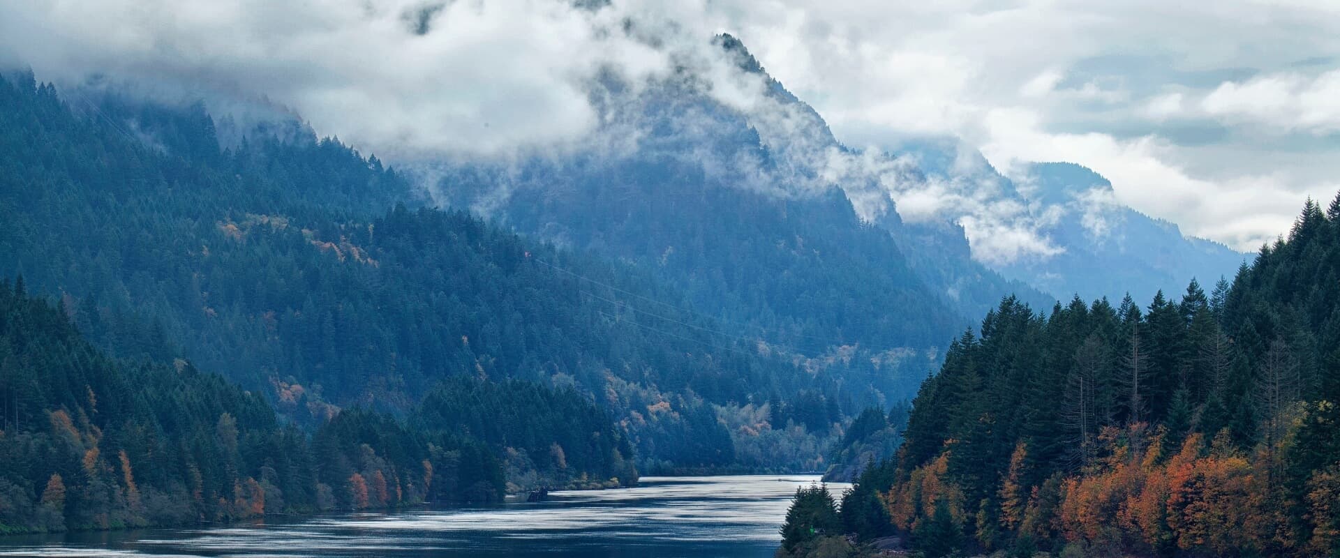 A tranquil river flows through a misty valley surrounded by mountains and dense forests.