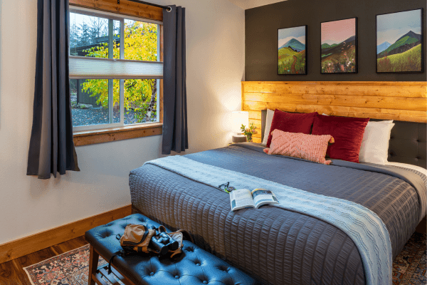 Cozy cabin bedroom with a neatly made bed, warm wood accents, soft lighting, and peaceful forest views through the window.