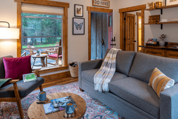Cabin living area with a sofa, fireplace, wood accents, and large windows with views of the trees.