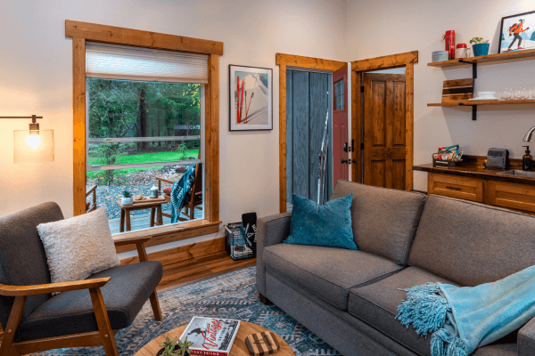 Cabin living area with a sofa, fireplace, wood accents, and large windows with views of the trees.