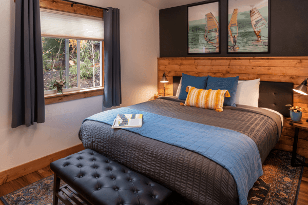 Cozy cabin bedroom with a neatly made bed, warm wood accents, soft lighting, and peaceful forest views through the window.