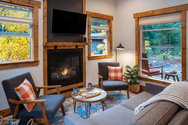 Warm and inviting cabin living room with a fireplace, cozy seating, and large windows framing peaceful forest views.