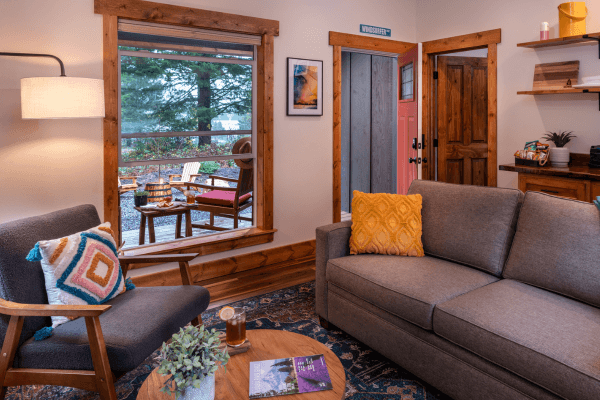Cabin living area with a sofa, fireplace, wood accents, and large windows with views of the trees.