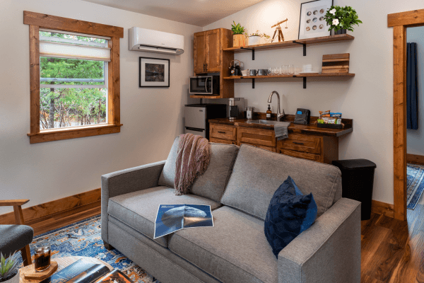 Cabin living area with a sofa, kitchenette, wood finishes, and a window overlooking the trees.