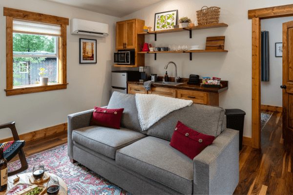 Cabin living area with a sofa, kitchenette, wood finishes, and a window overlooking the trees.