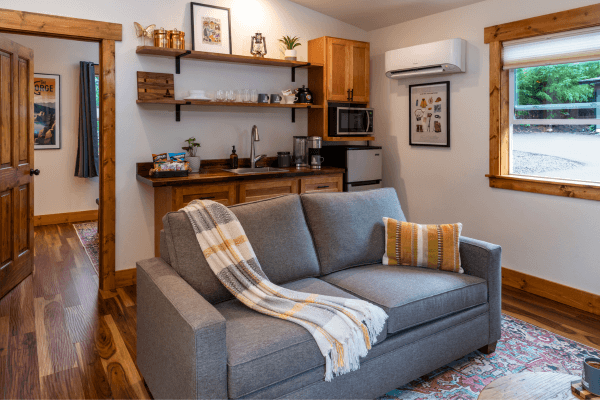 Cabin living area with a sofa, kitchenette, wood finishes, and a window overlooking the trees.