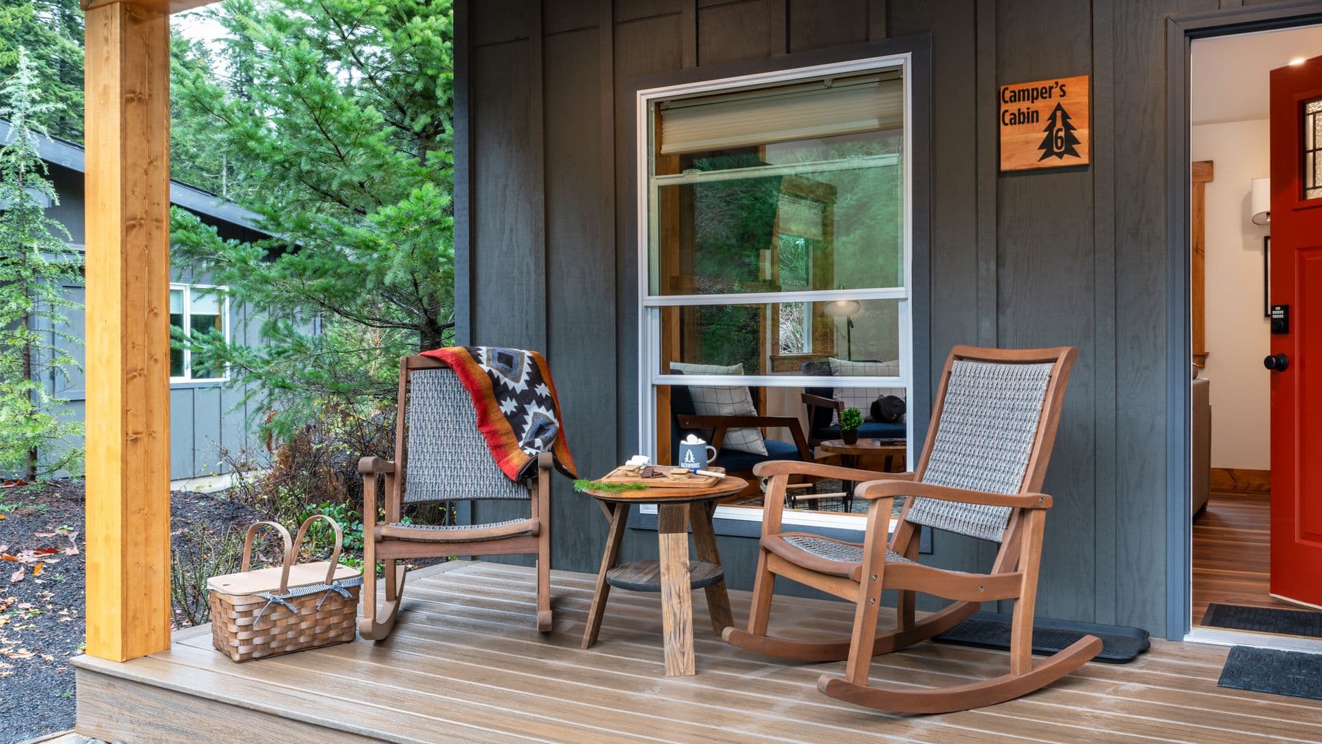 A cozy porch with rocking chairs, a small table, and a basket, surrounded by greenery.