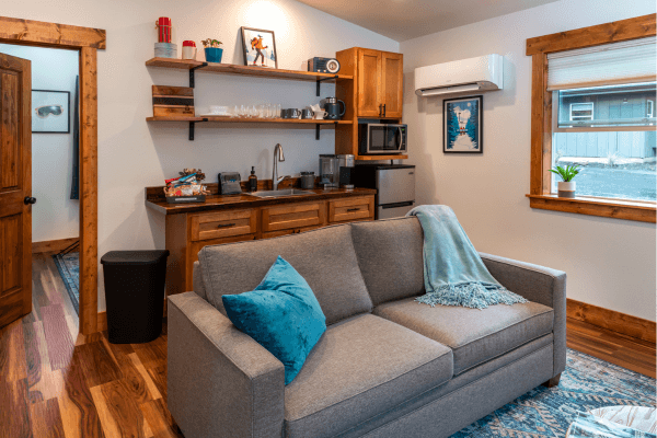 Cabin living area with a sofa, kitchenette, wood finishes, and a window overlooking the trees.