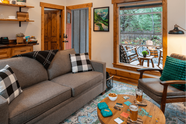 Cabin living area with a sofa, fireplace, wood accents, and large windows with views of the trees.