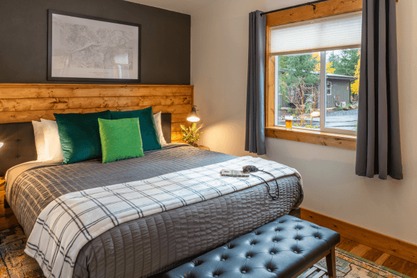 Cozy cabin bedroom with a neatly made bed, warm wood accents, soft lighting, and peaceful forest views through the window.