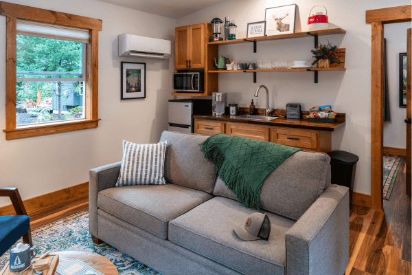 Cabin living area with a sofa, kitchenette, wood finishes, and a window overlooking the trees.