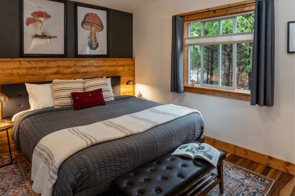 Cozy cabin bedroom with a neatly made bed, warm wood accents, soft lighting, and peaceful forest views through the window.