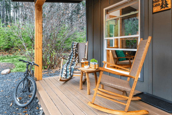 Cozy cabin porch with wooden chairs, bright blue paddles, and peaceful views of trees.