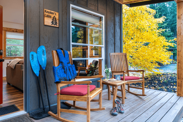 Cozy cabin porch with wooden chairs and peaceful views of golden autumn trees.