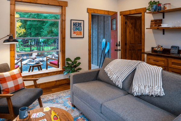 Cabin living area with a sofa, fireplace, wood accents, and large windows with views of the trees.