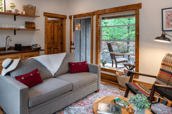 Cabin living area with a sofa, fireplace, wood accents, and large windows with views of the trees.