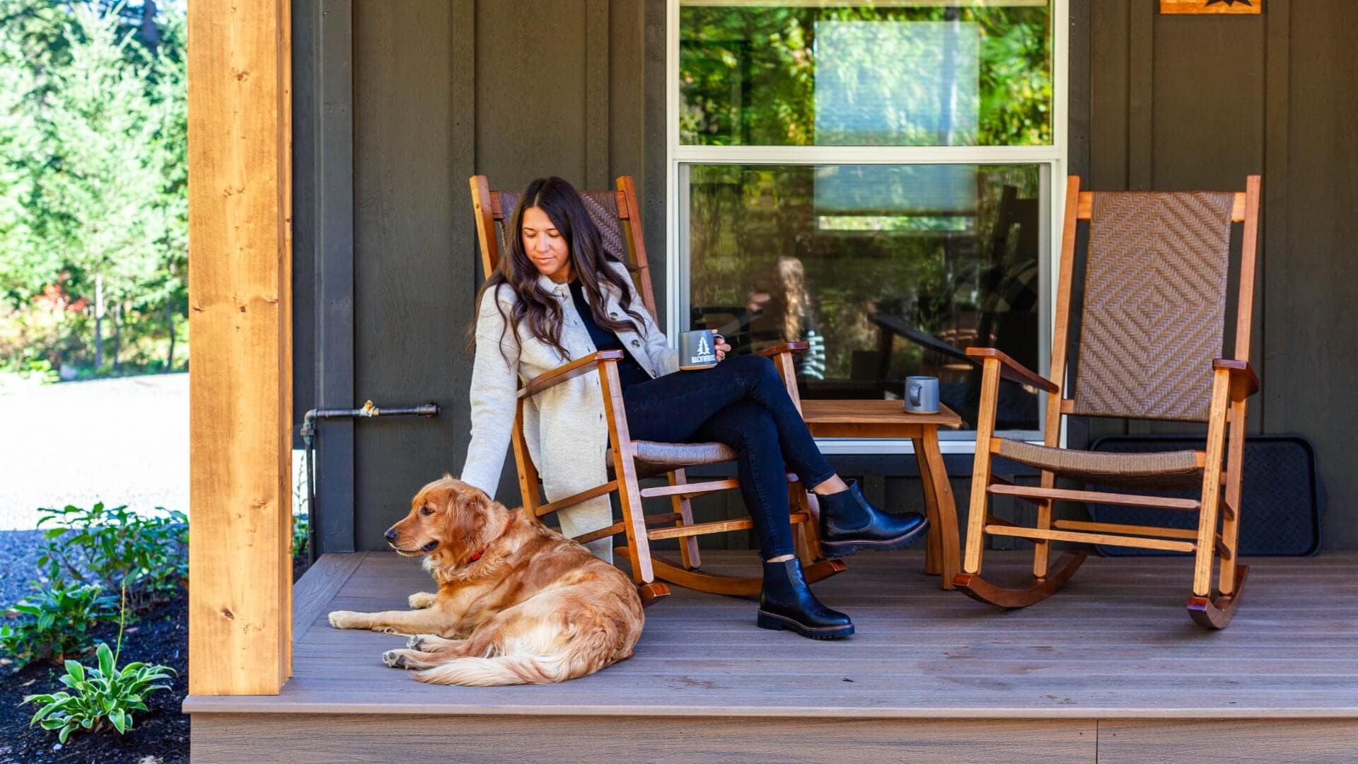 A woman sits on a porch, petting a golden retriever beside her, with rocking chairs in the background.