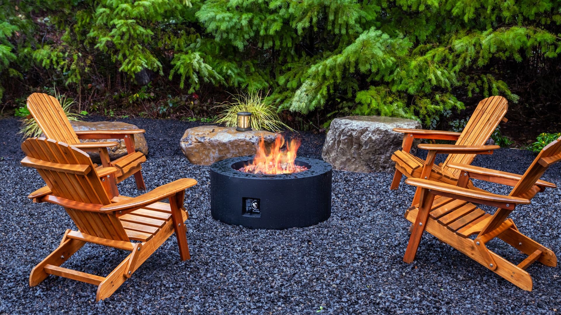 A cozy outdoor fire pit surrounded by wooden chairs and gravel.