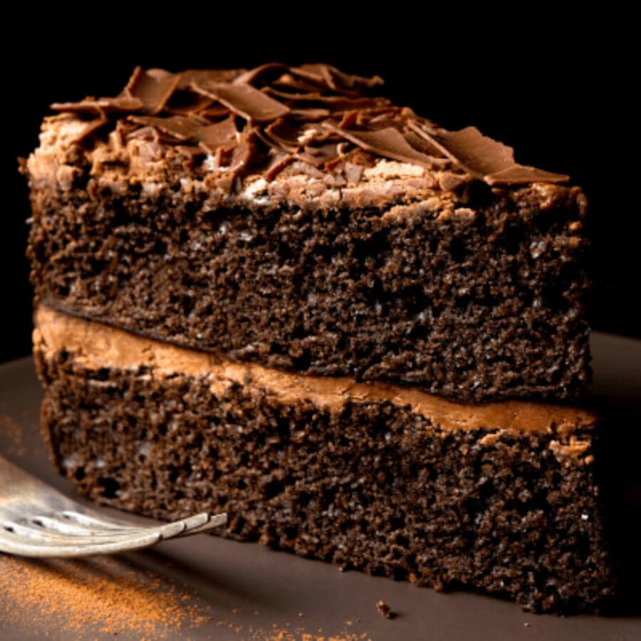 A slice of chocolate cake with creamy frosting and chocolate shavings on top.