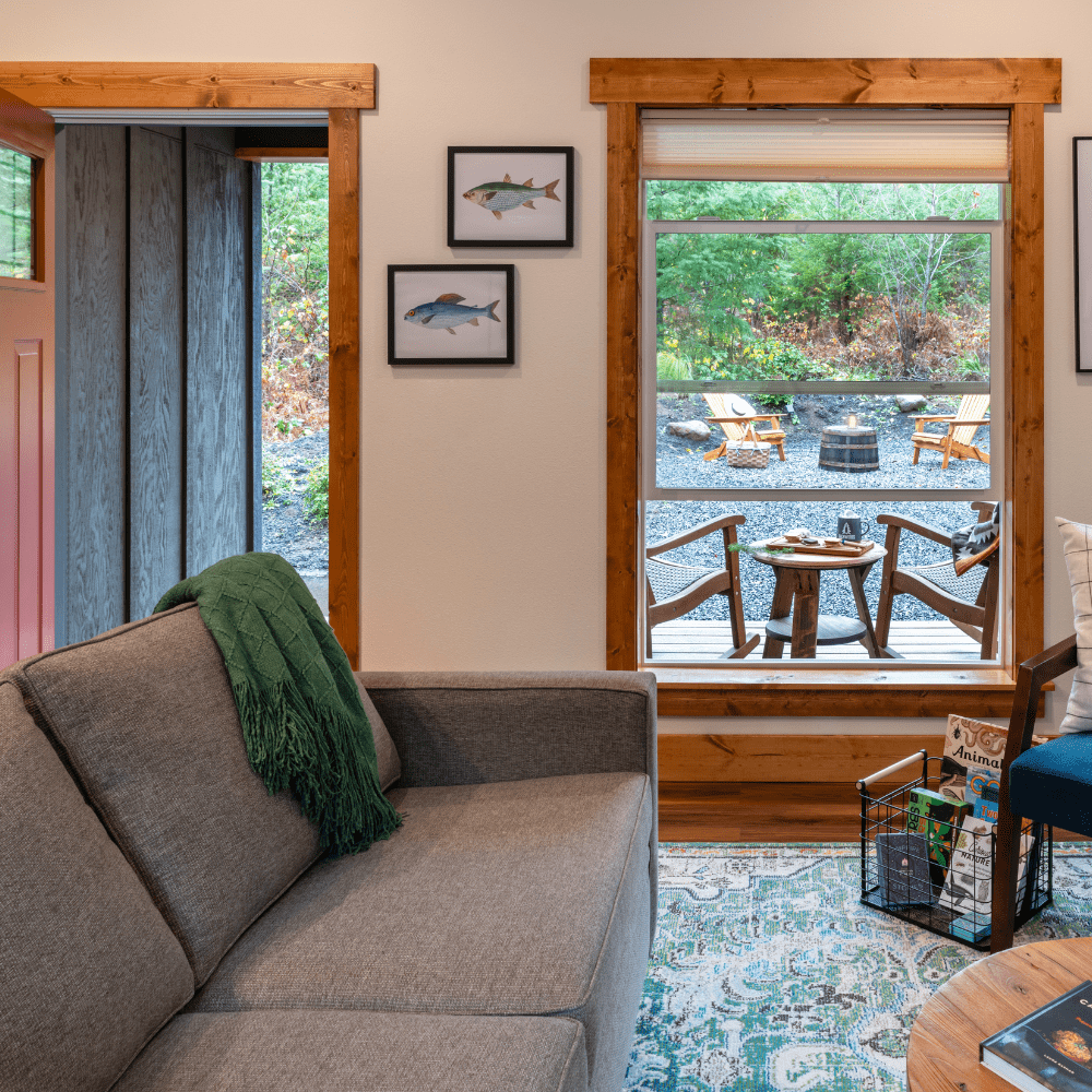 IMAGE OF SOFA AND VIEW OUT WINDOW TO ROCKING CHAIRS OF CAMPER'S CABIN AT BACKWOODS CABINS