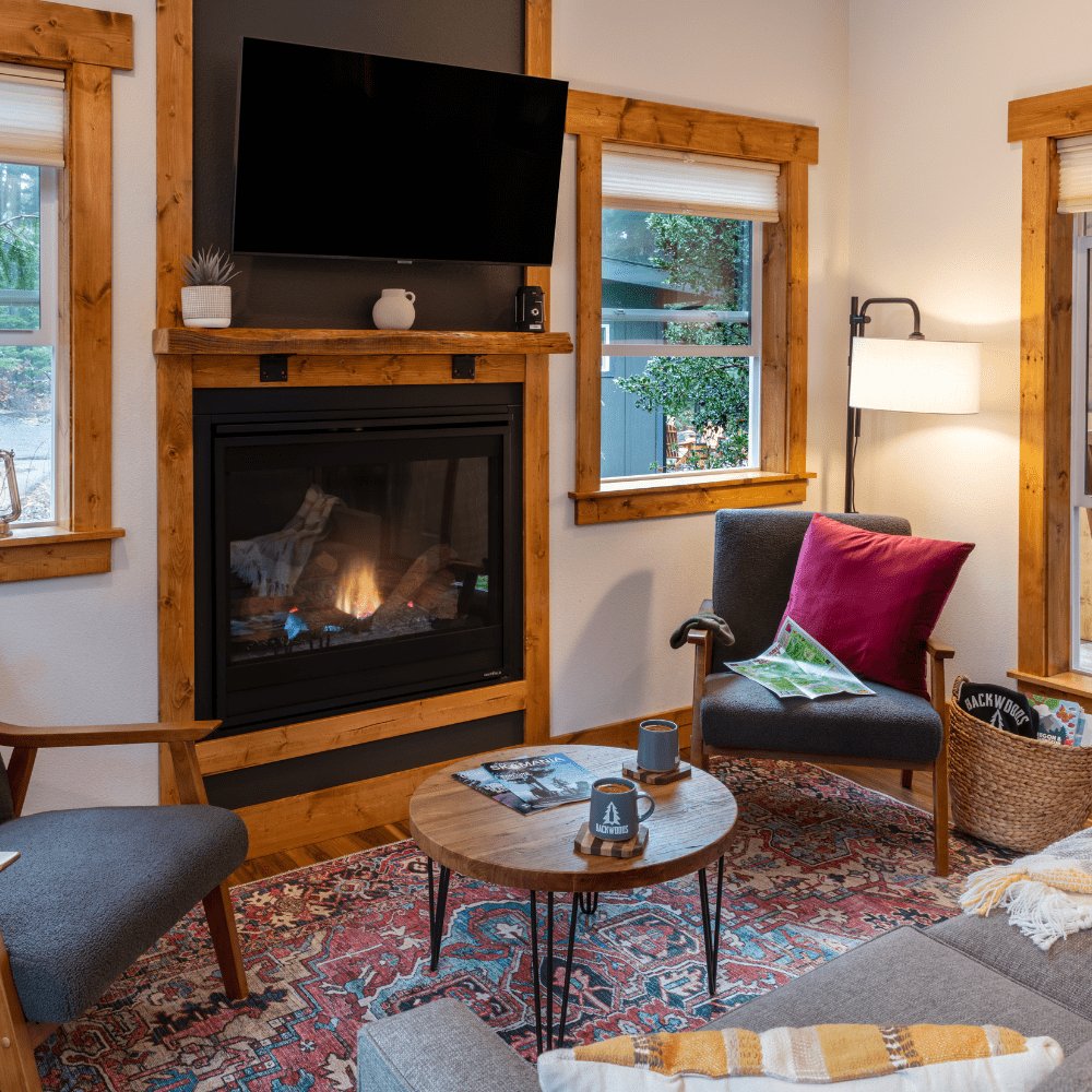 Image of gas fireplace, loveseat and twon chair with view out of windows to forest scene in the Cascade Mountains at Backwoods Cabins in Carson, Washington