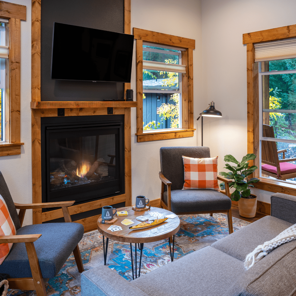 Image of gas fireplace, loveseat and twon chair with view out of windows to forest scene in the Cascade Mountains at Backwoods Cabins in Carson, Washington