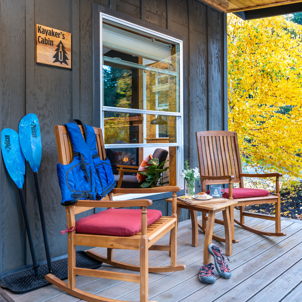 Image of front porch cabin with two rocking chairs, coffee mug, and kayak paddles