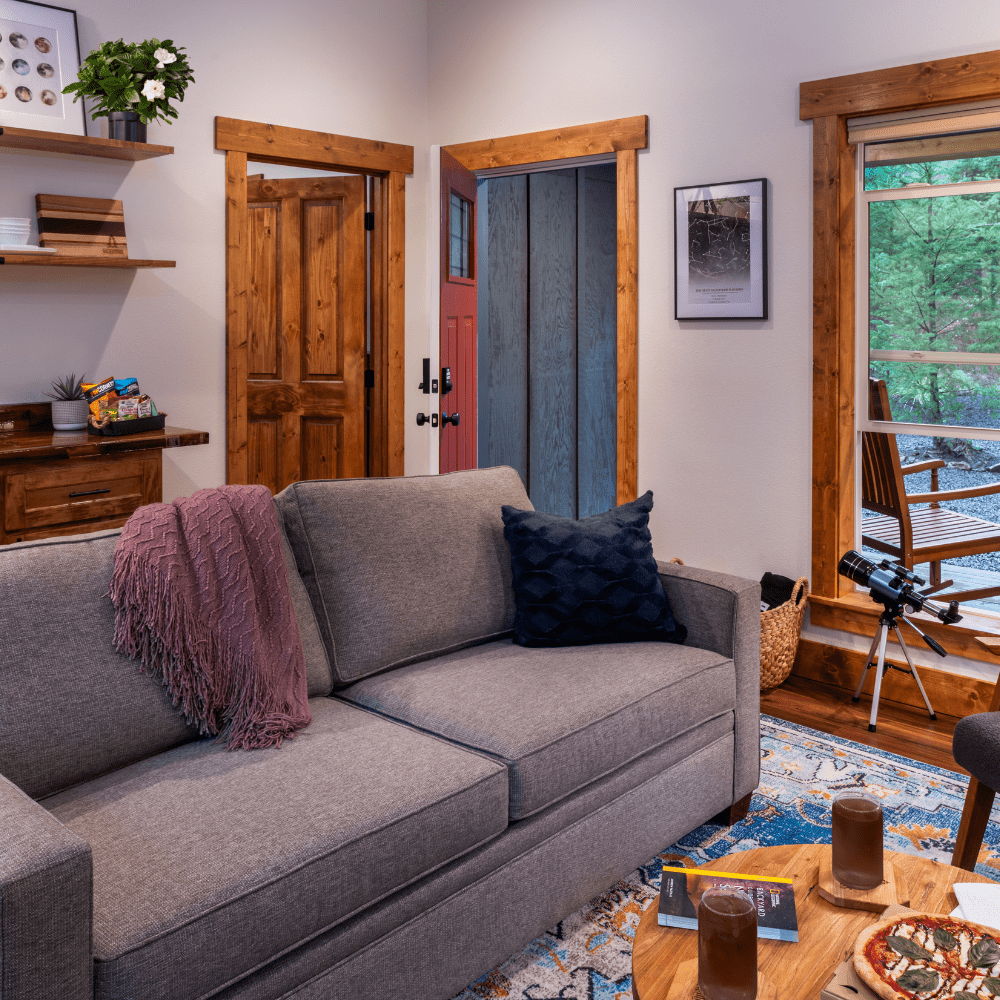 Image of grey couch with telescope at the window looking out into the forest at the Stargazers cabin at Backwoods Cabins